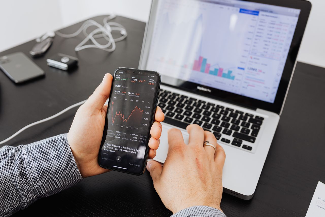 why-choose-us Person analyzes stock data with a smartphone and laptop, indoors.